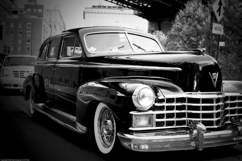 Un auto clásico en una calle de la ciudad, fotografiado en blanco y negro